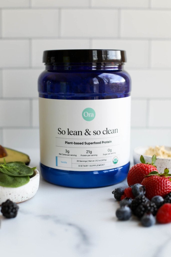 A jar of Ora vanilla plant based protein powder with a subway tiled background for a plant-based protein powder round-up.