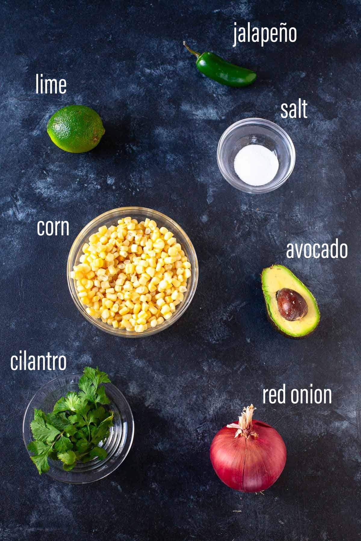 corn avocado salsa ingredients laid out on dark grey surface with white text overlay