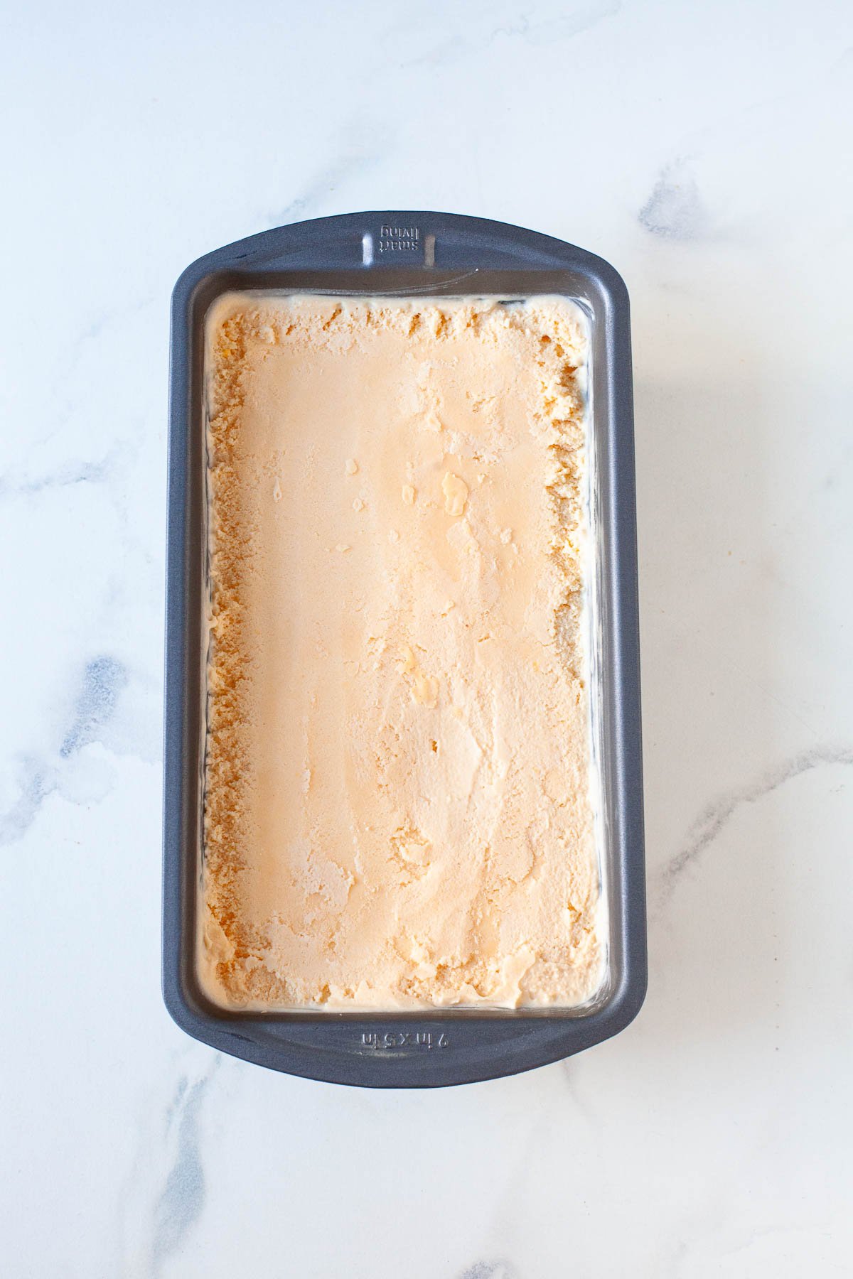 hard peach ice cream frozen in gray loaf pan on marble surface
