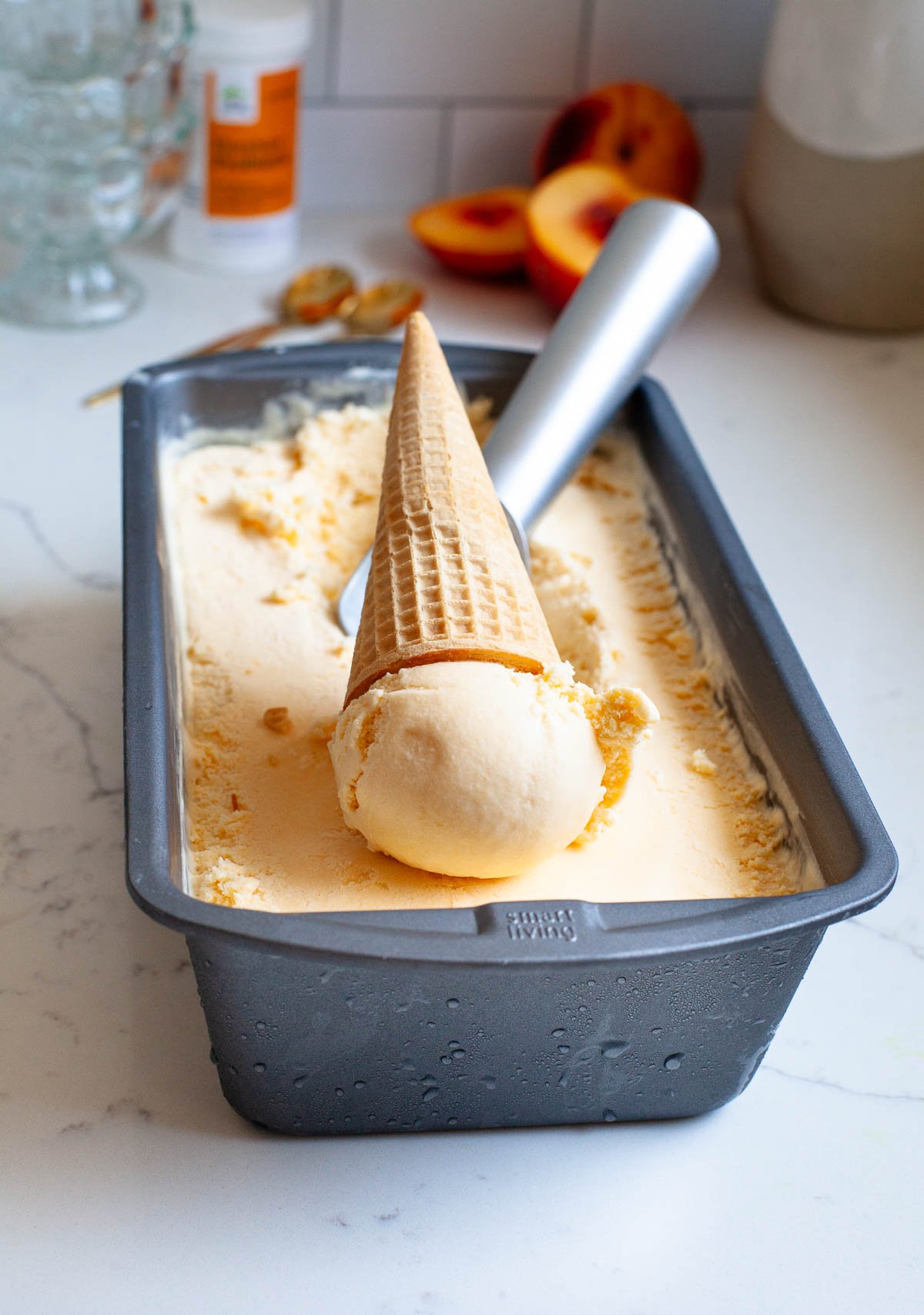 hard peach ice cream in gray loaf pan with one scoop in a sugar cone