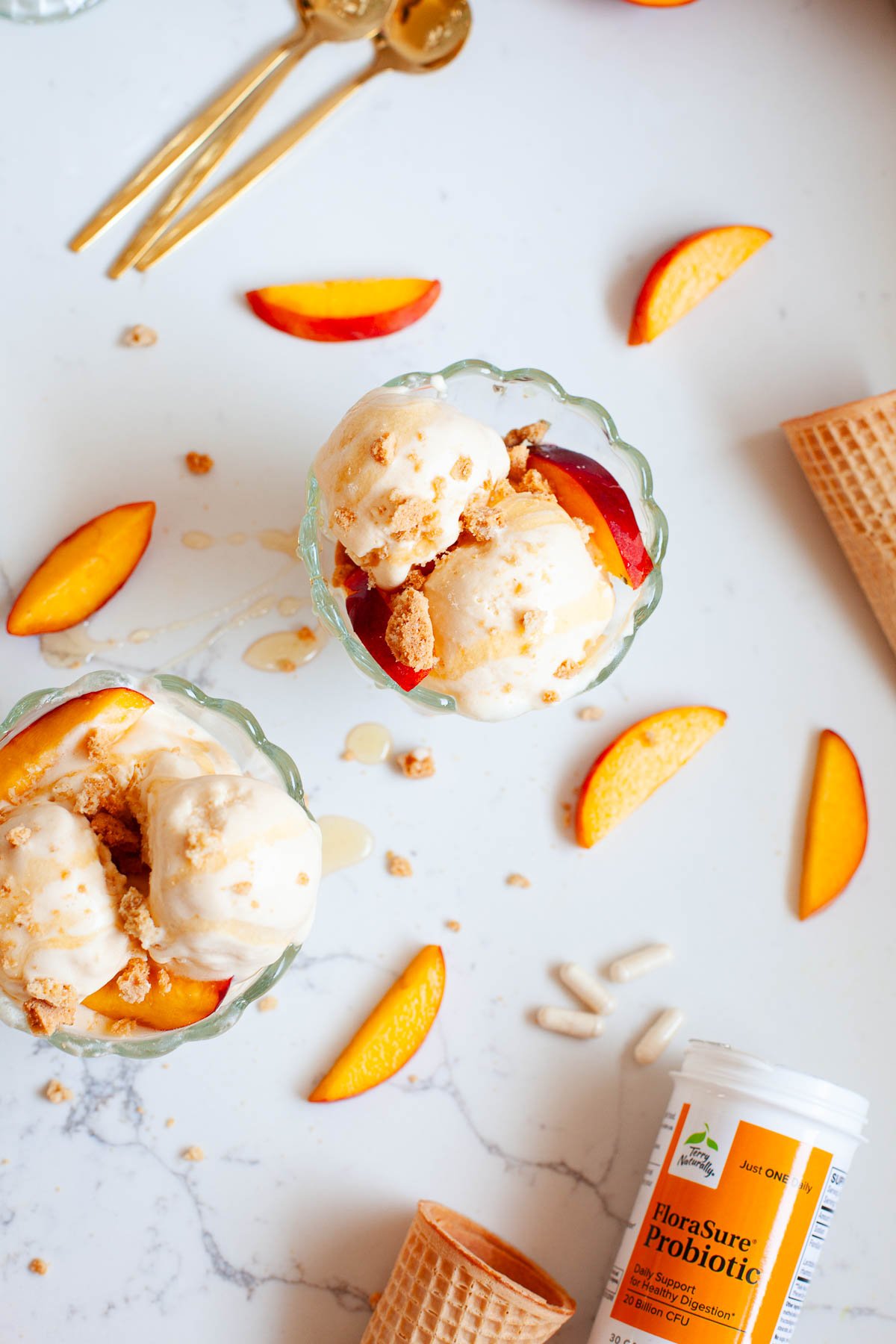 two sundae bowls with peach ice cream, sugar cones, peach slices, gold spoons, probiotic supplement